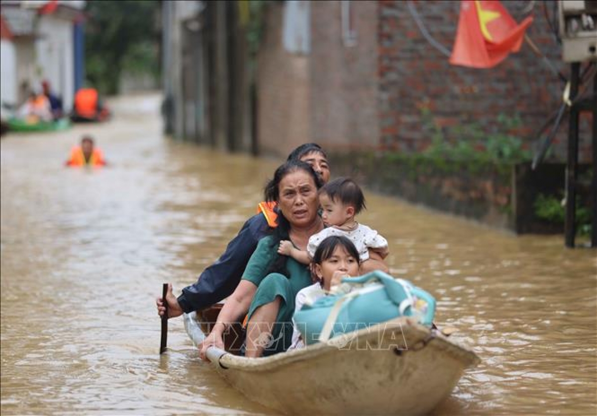 Bà Yến (thôn An Lạc) cùng các cháu được hỗ trợ di chuyển tới nơi an toàn. Ảnh: Thanh Tùng (TTXVN)